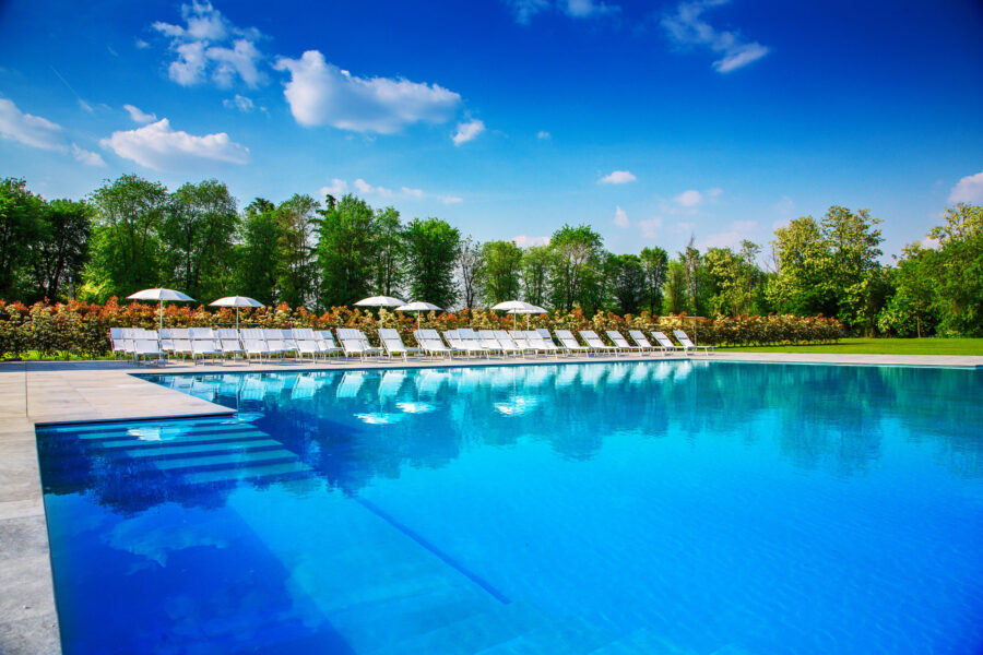 Immagine che ritrae la piscina all'aperto di Villa Sant'Uberto con degli ombrelloni e lettini sullo sfondo.