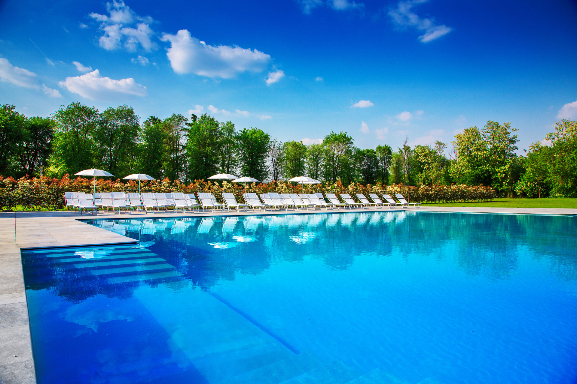 Immagine che ritrae la piscina all'aperto di Villa Sant'Uberto con degli ombrelloni e lettini sullo sfondo.