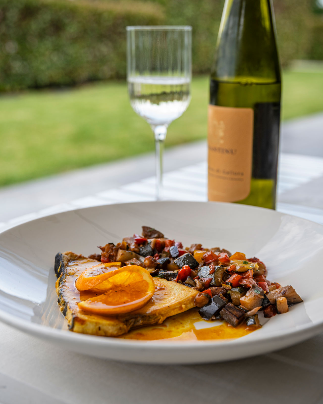 Immagine che mostra un piatto di pesce con una bottiglia di vino serviti al Restaurant di Villa Sant'Uberto